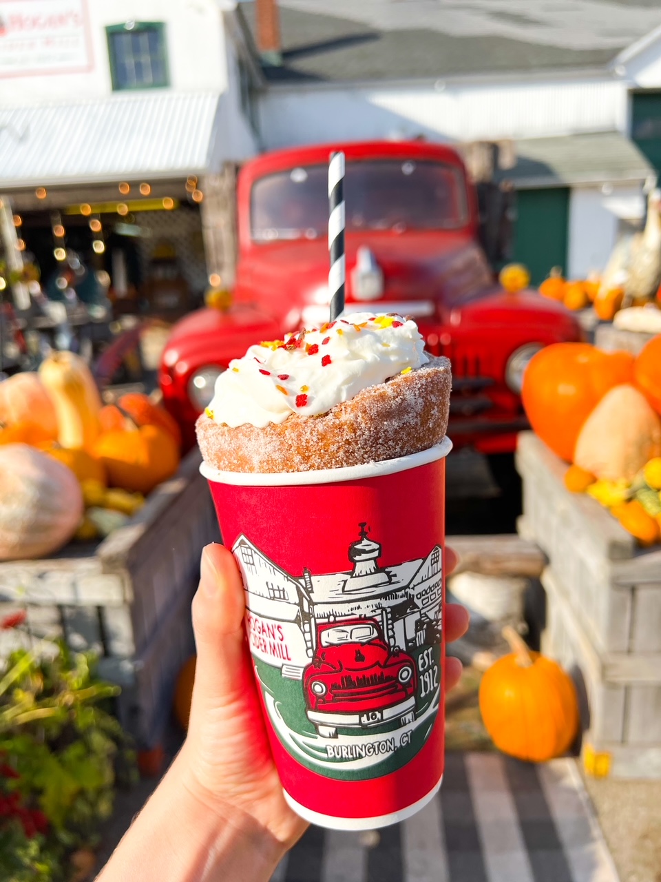 woman holding fall themed drink in front of pumpkins