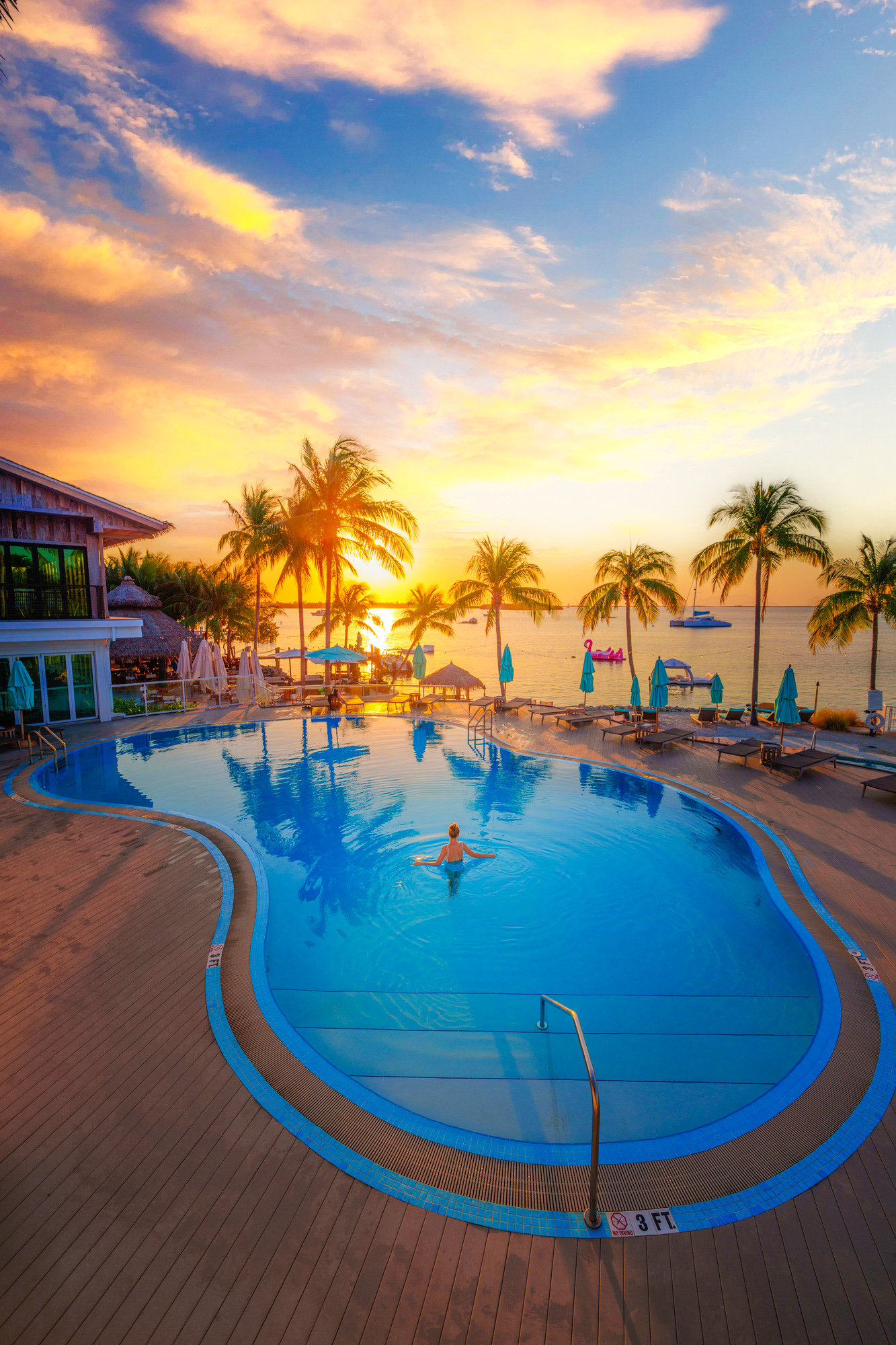 woman standing in pool at sunset with palm trees behind her