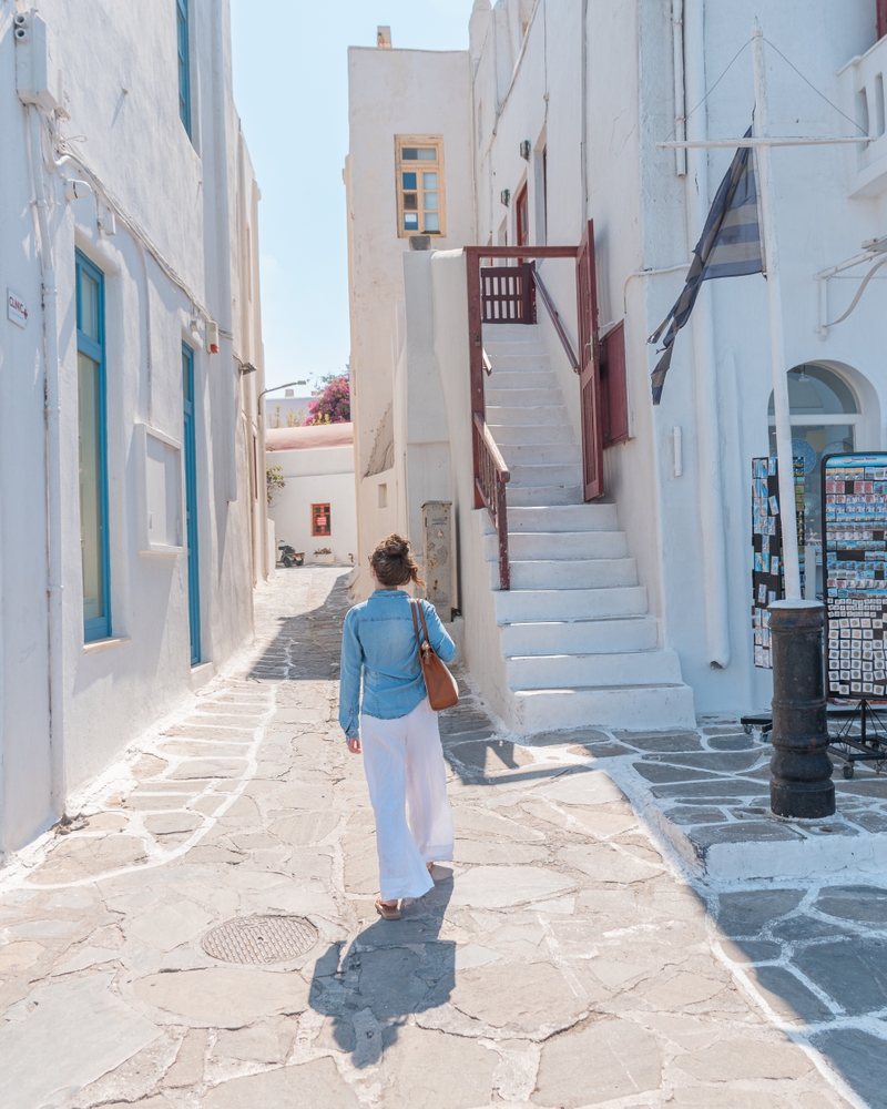 Woman walking down n alley in Greece wearing loose, linen pants and a denim shirt.