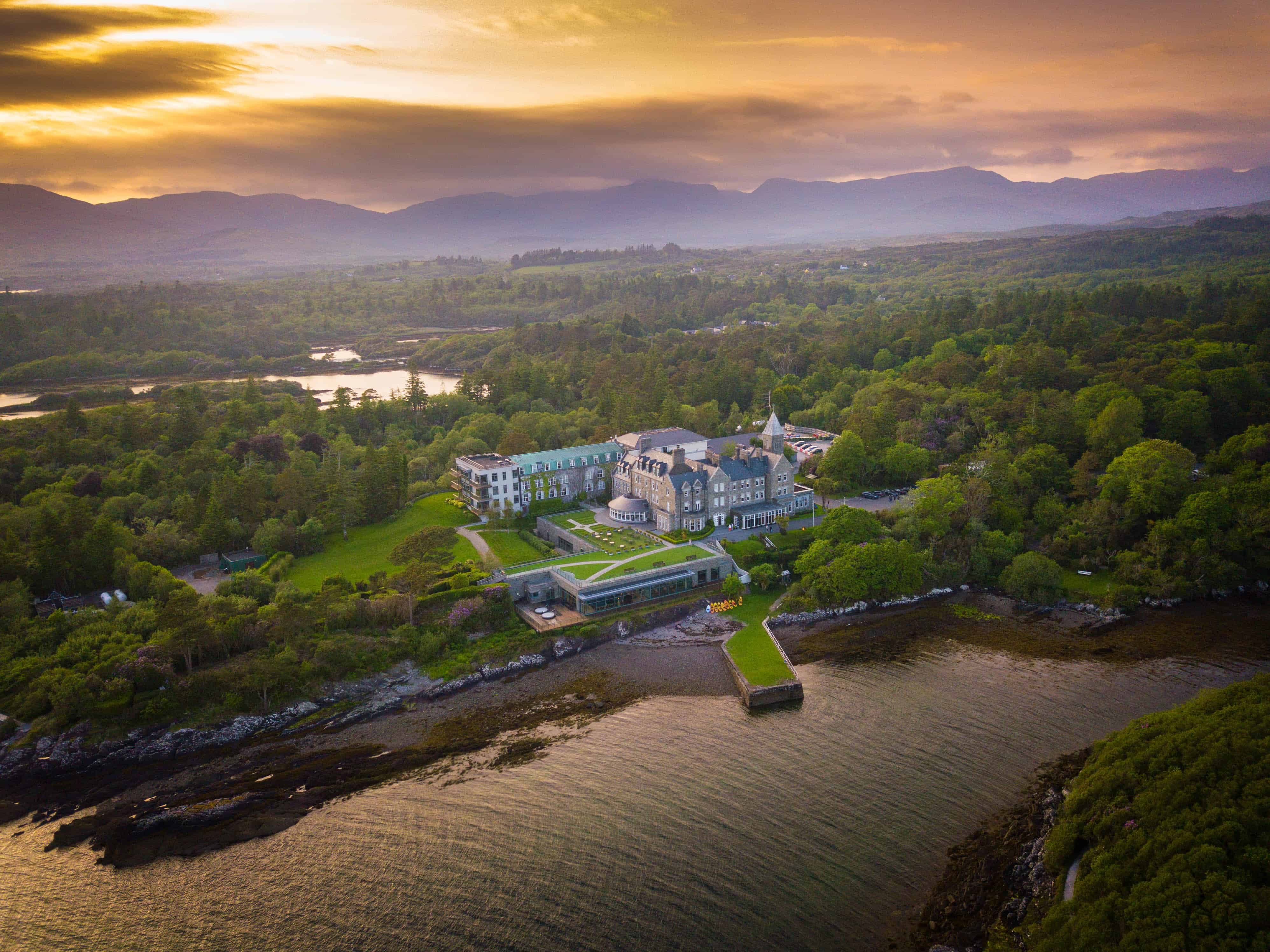 Sunset aerial photo of the Parknasilla Resort & Spa on the water with green trees all around.