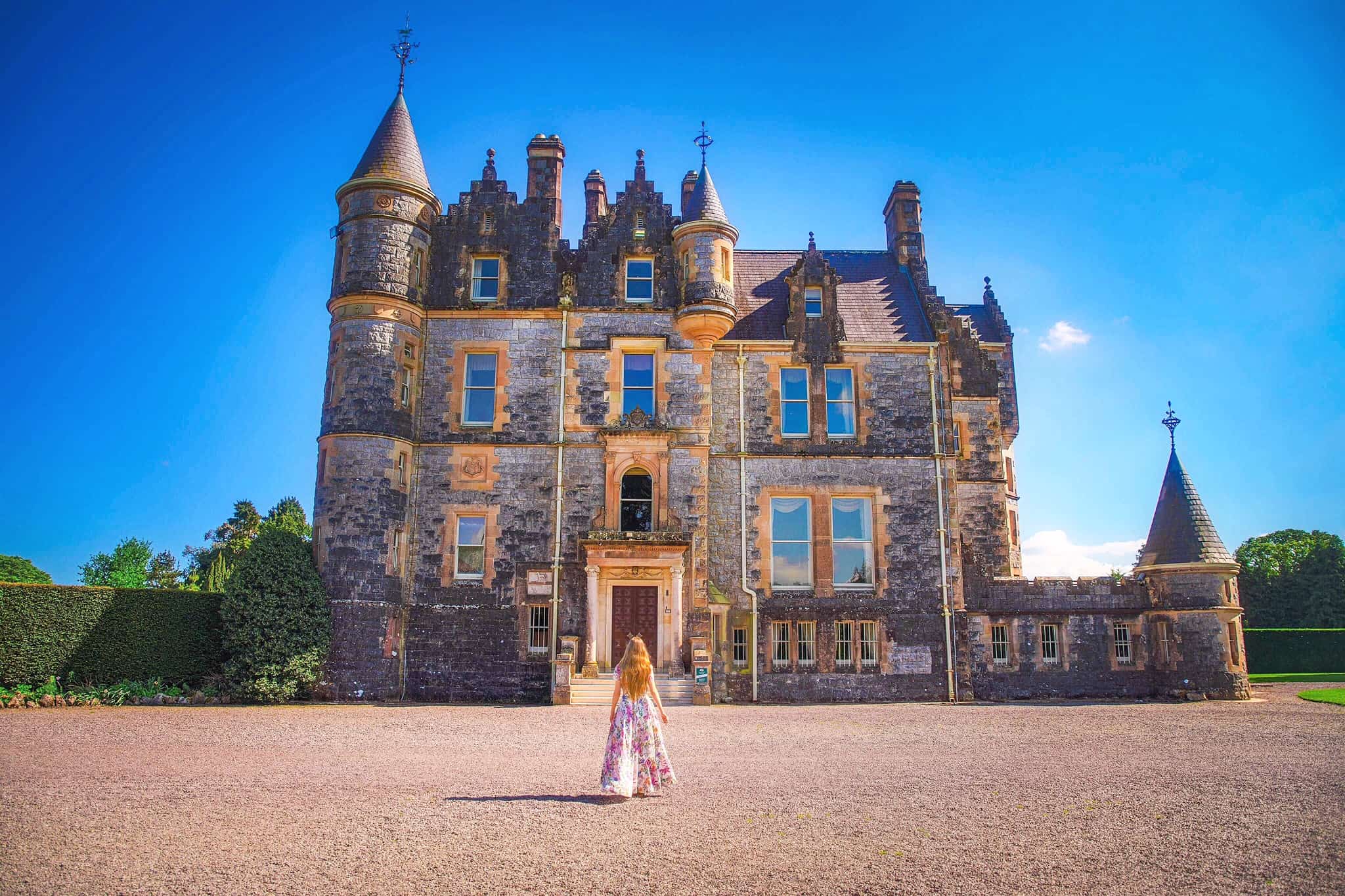 Woman in a dress in front of the stone Blarney Castle House on a sunny day.