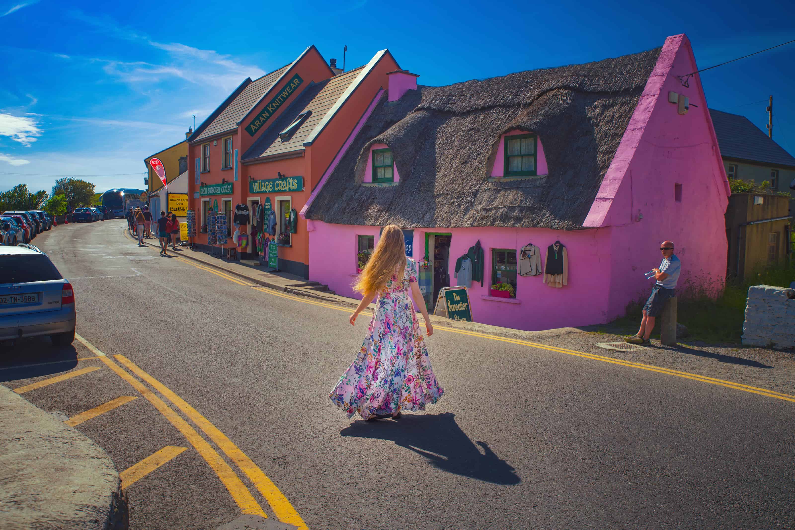 Woman in a flowing floral dress walking down the street in Doolin next to colorful buildings.