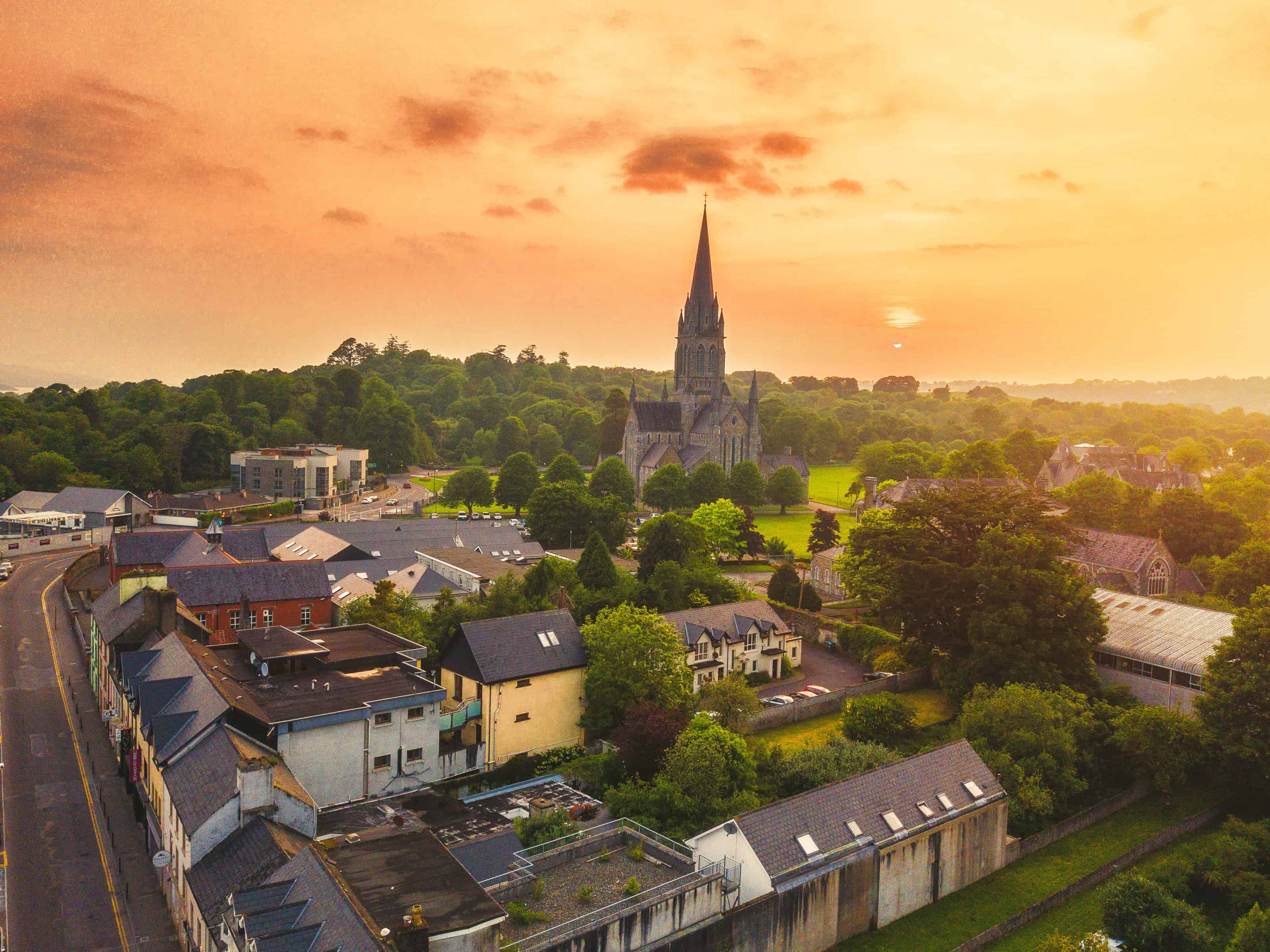 Aerial view of an orange sunset over the quaint town of Killarney with a church on an Ireland road trip.