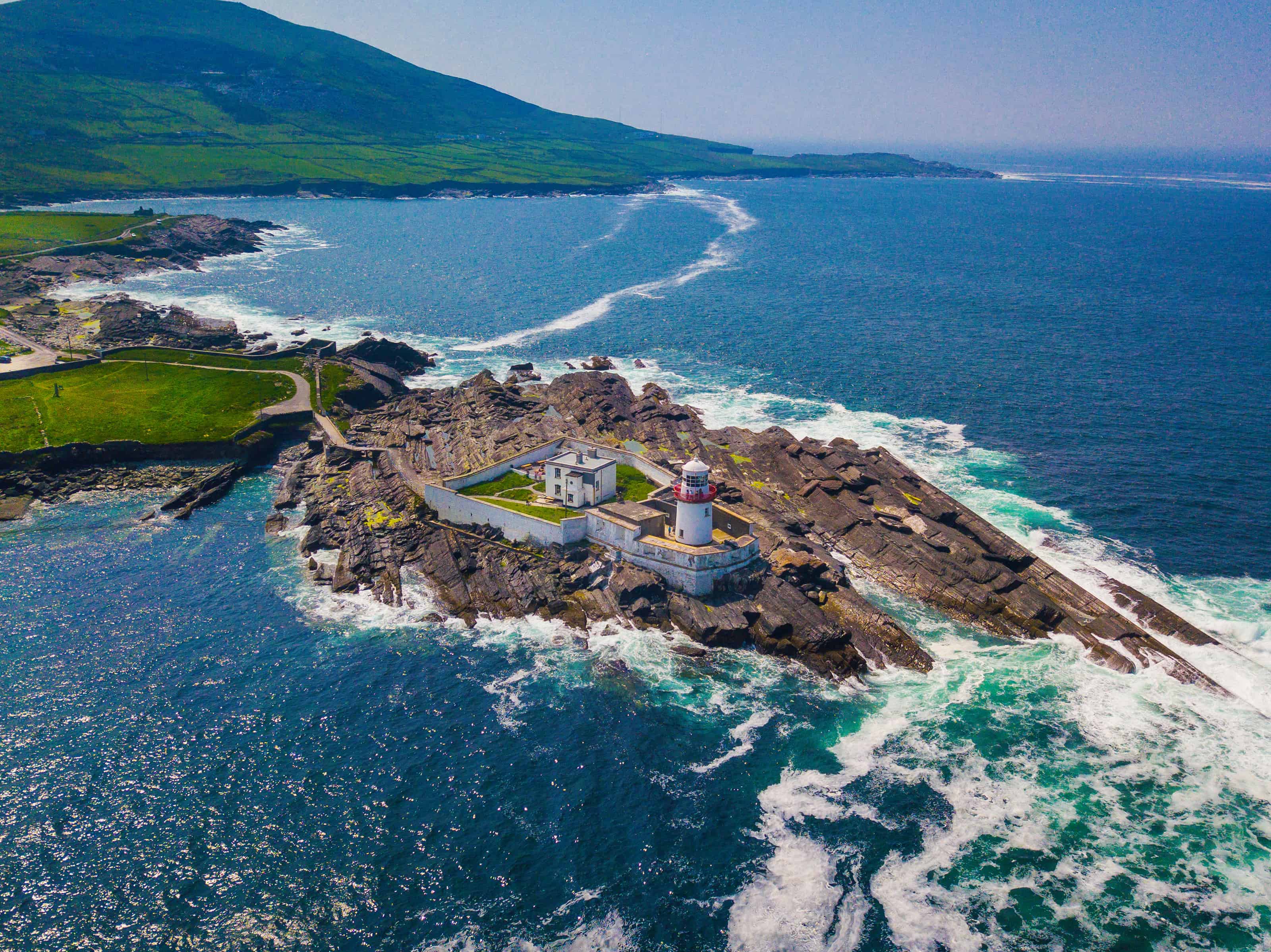 Aerial image of a white lighthouse on a rugged rock outcropping on Valentia Island.