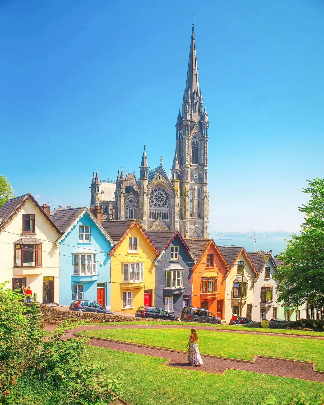 Woman in a dress in front of the colorful card houses and the cathedral in Cobh, Ireland.