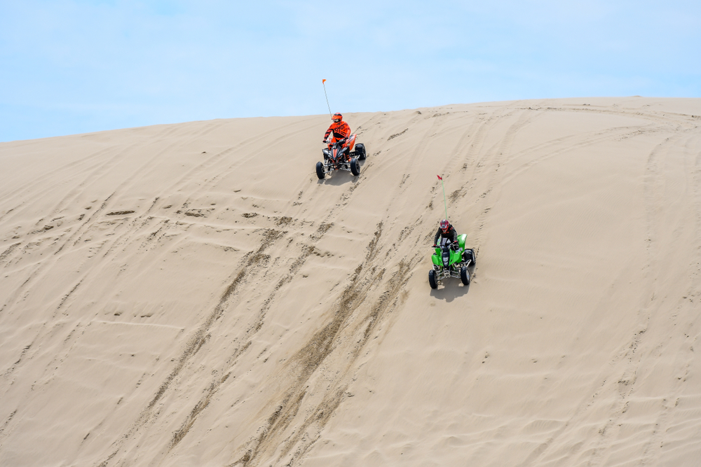 Two brightly colored off road vehicles driving the sand dunes at Oregon Dunes National Recreational Area on an Oregon road trip.