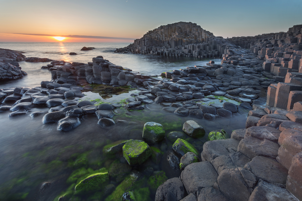 Sunset at Giant's Causeway with black, basalt columns in the water.