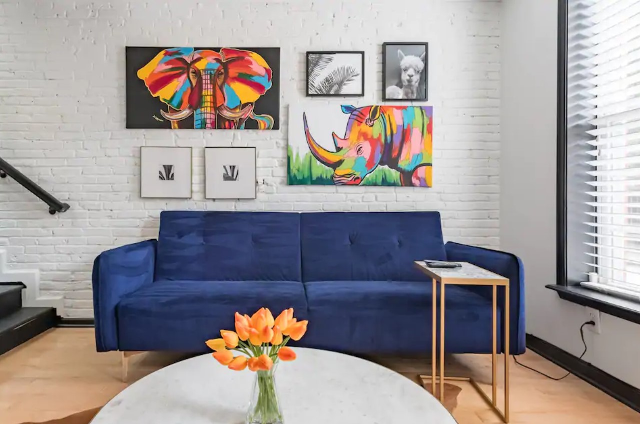 Dark blue sofa against a white brick wall with vibrant paintings on it one of the best airbnbs in baltimore