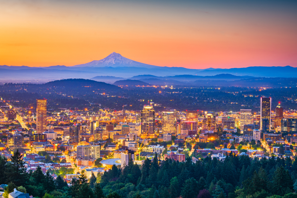 Vivid orange sunset over the lit-up city of Portland with mount hood in the background.