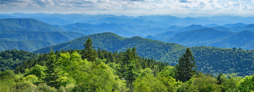 arial view of blue ridge parkway during the day, with endless mountain range views and greenery surrounding the mountains 