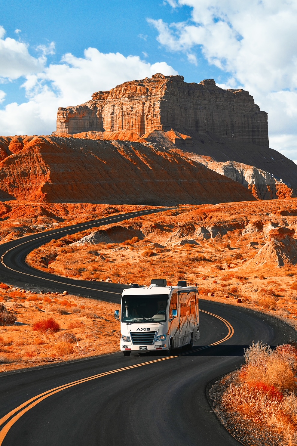 RV driving down a twisting road in a rugged, red colored Utah landscape during a Utah road trip.