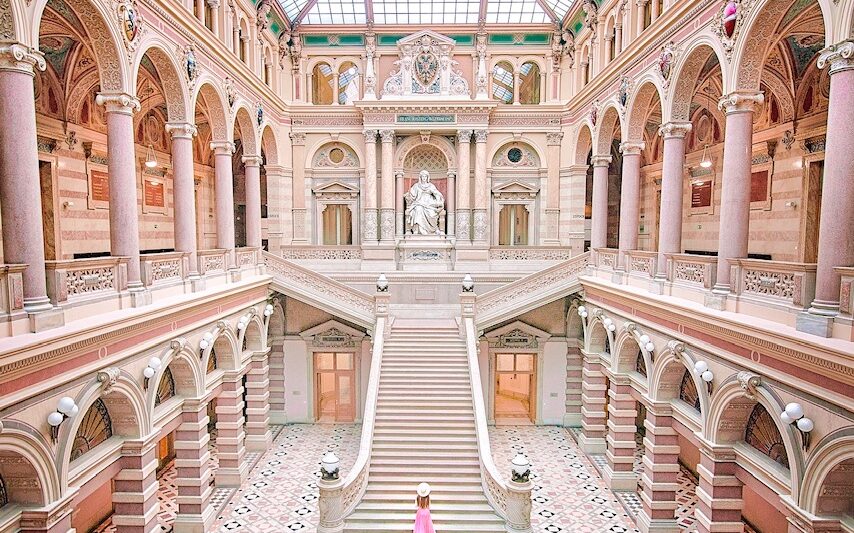 woman standing in a pink skirt on stairs in vienna austria. the whole scene is indoors with a glass roof