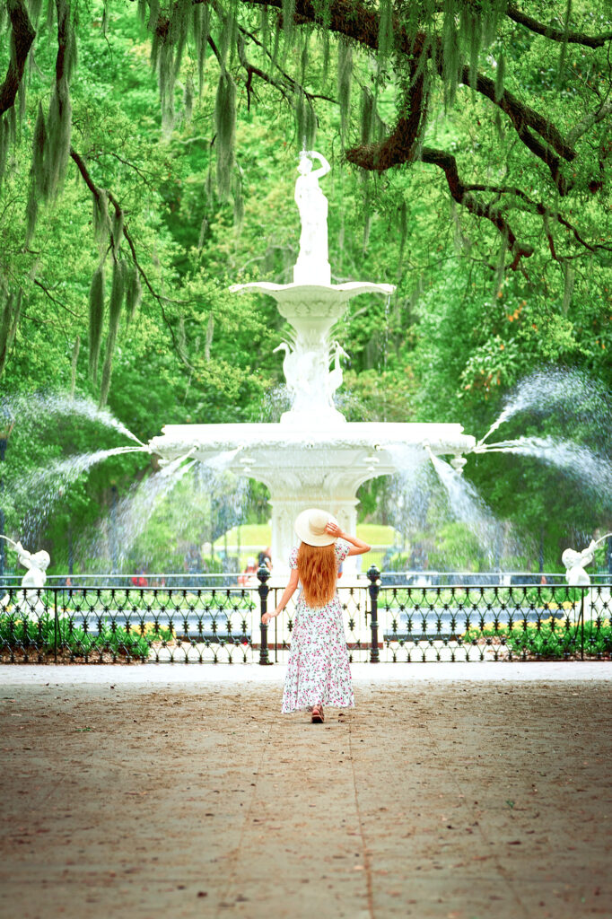 woman with a hat in front of a fountain in Savannah. 