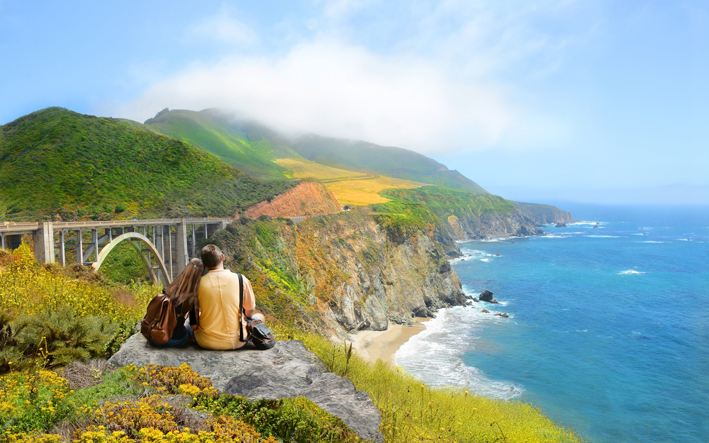 Couple looking at beautiful coastal mountain landscape on hiking trip. Bixby Bridge, Big Sur, California, USA.