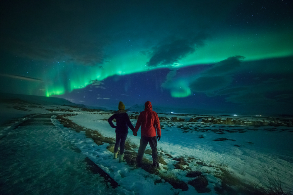 Couple watches the northern lights. Woman and man at winter night landscape . Iceland. One of the best vacation spots for couples.