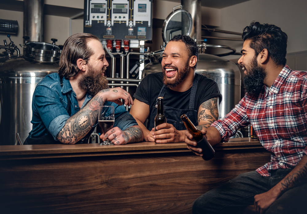 Three male friends laughing together over a beer during a 30th birthday trip to Boulder CO. 