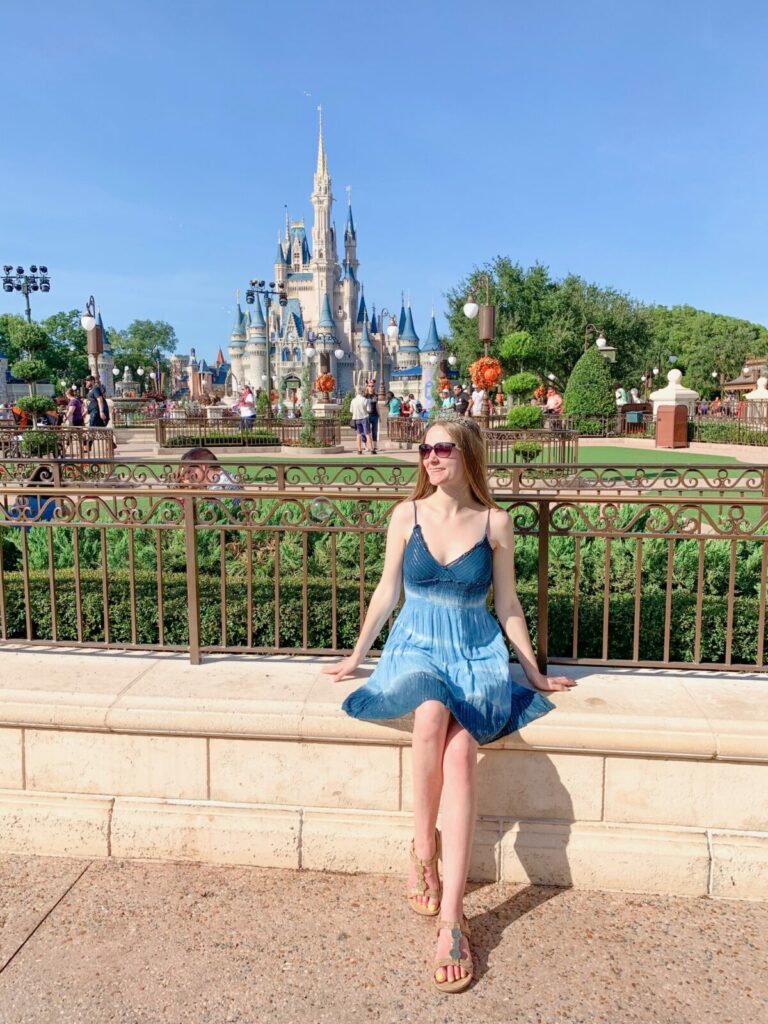 Me in a blue dress sitting in front of the Cinderella's Castle at Magic Kingdom in Walt Disney World, one of the best 30th birthday trip ideas for women.