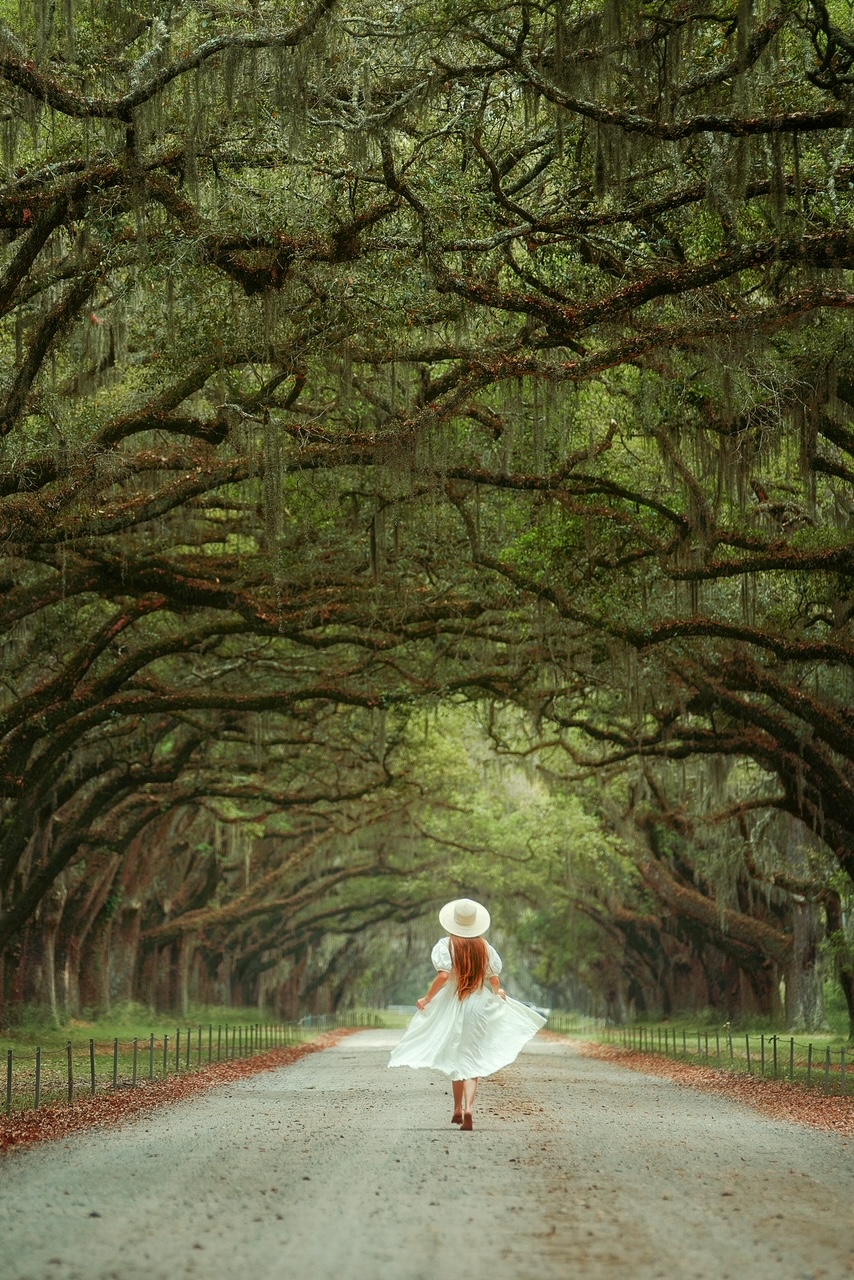 Me in a white dress running down a gravel road with trees lining either side and Spanish moss hanging down in Savannah Georgia, one of the best 30th birthday destinations. 