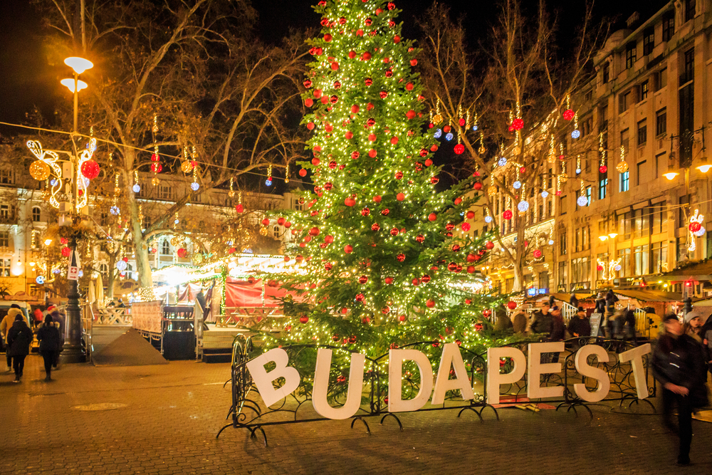 Budapest welcomes tourists and locals to its Christmas celebration with a sign that reads the city's name, a huge tree, and lights around the town square. 