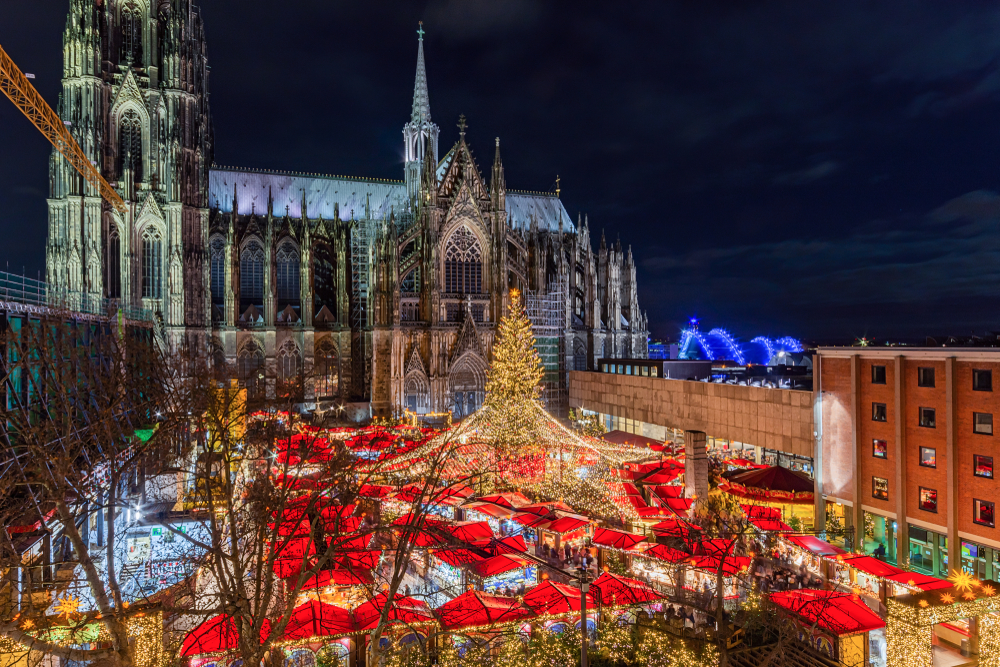 An arial shot of Cologne shows the red tops of tents and huts during the Christmas market that pops up with lights and trees outside the local church.