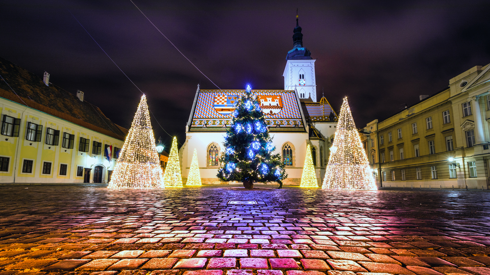 In front of a local church in Zagreb, a real Christmas tree is surrounded by fake-light Christmas trees that bring brightness to the square. 