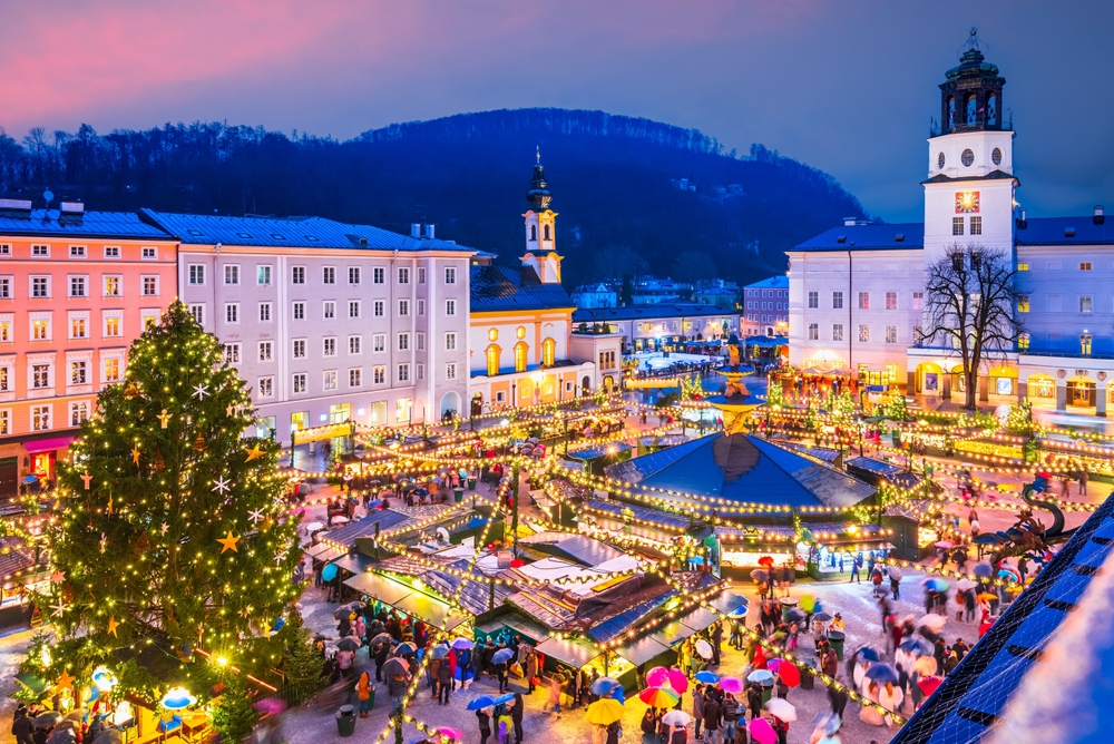 An arial shot of a traditional Christmas market shows one of the best Christmas cities in Europe as it lights up with stalls, string lights, trees and more. 