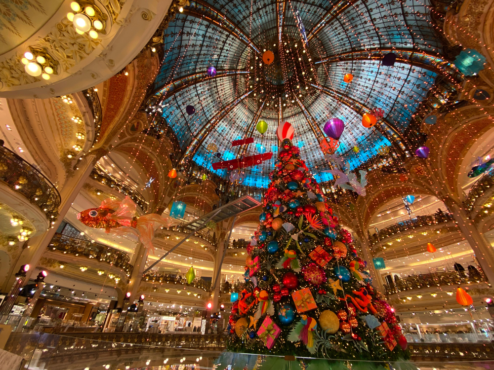 A giant shopping center with a dome features a huge Christmas tree and twinkling lights in Paris. 