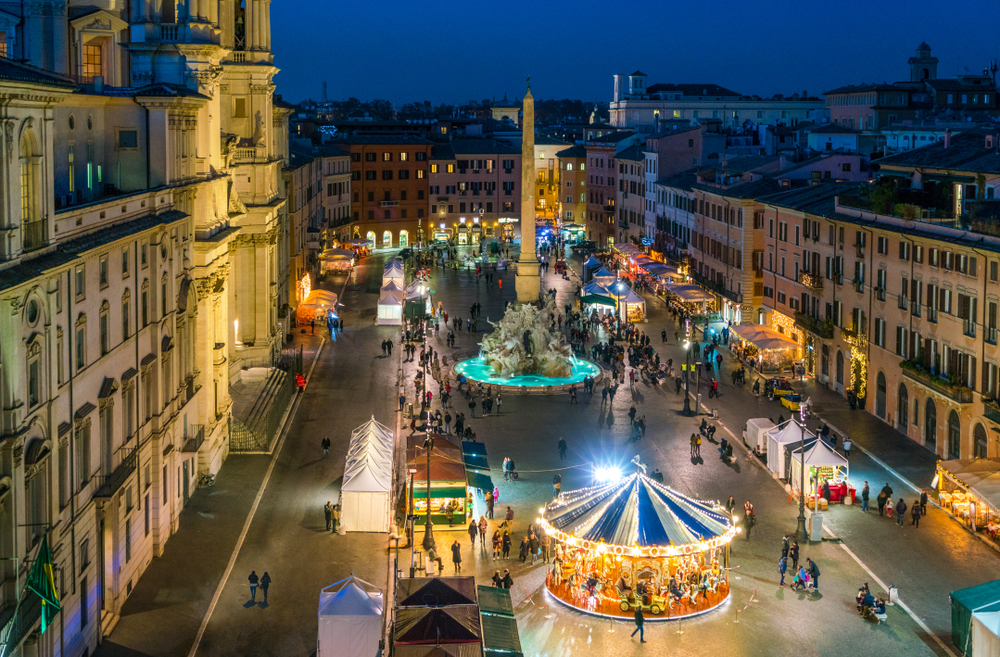 An arial shot of Rome shows the beginnings of Christmas markets: carousels, fountains, huts and people line the streets that are light up. 