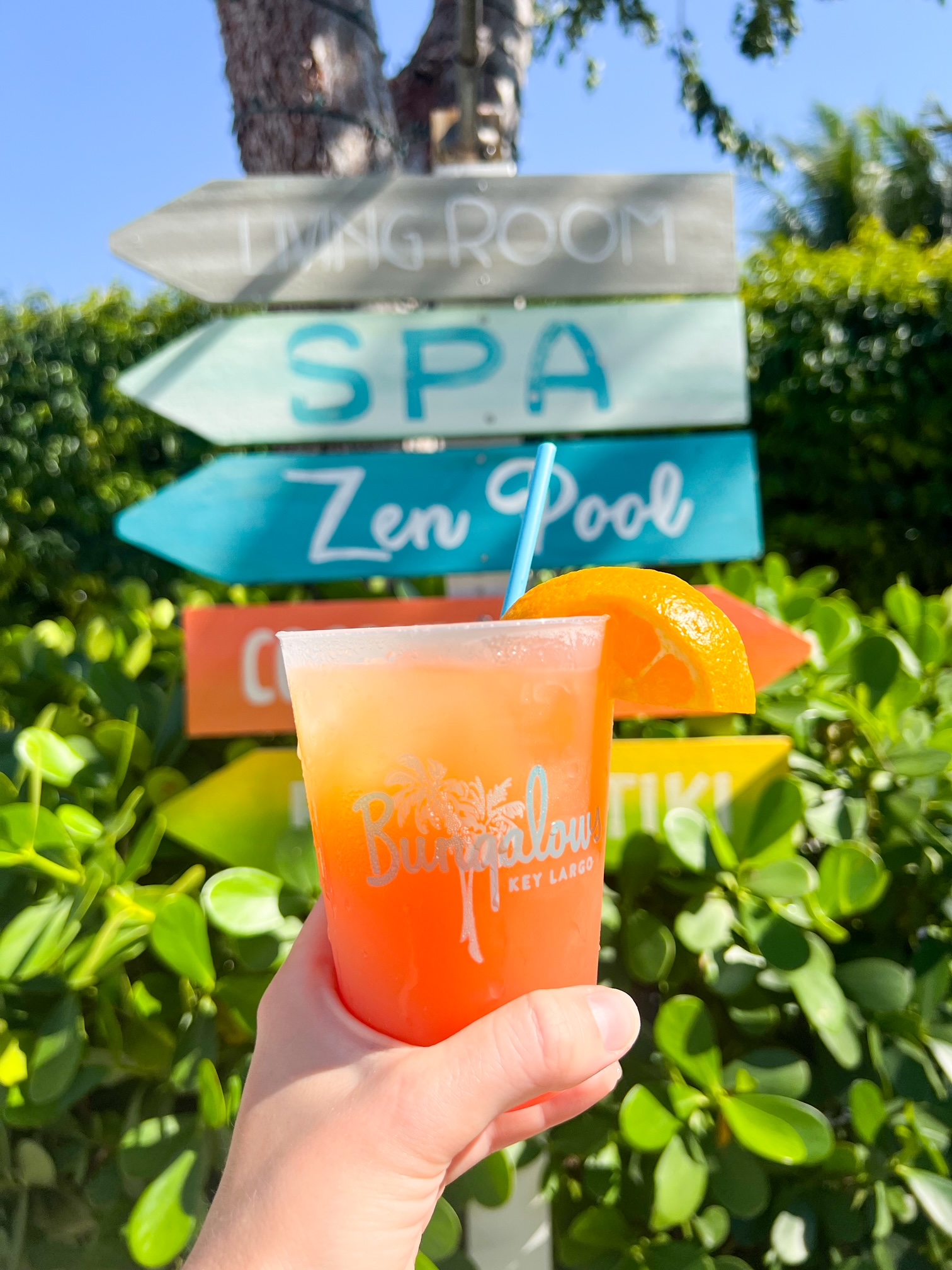 a girl holding a drink overlooking a sign with the directory of the spa and pools