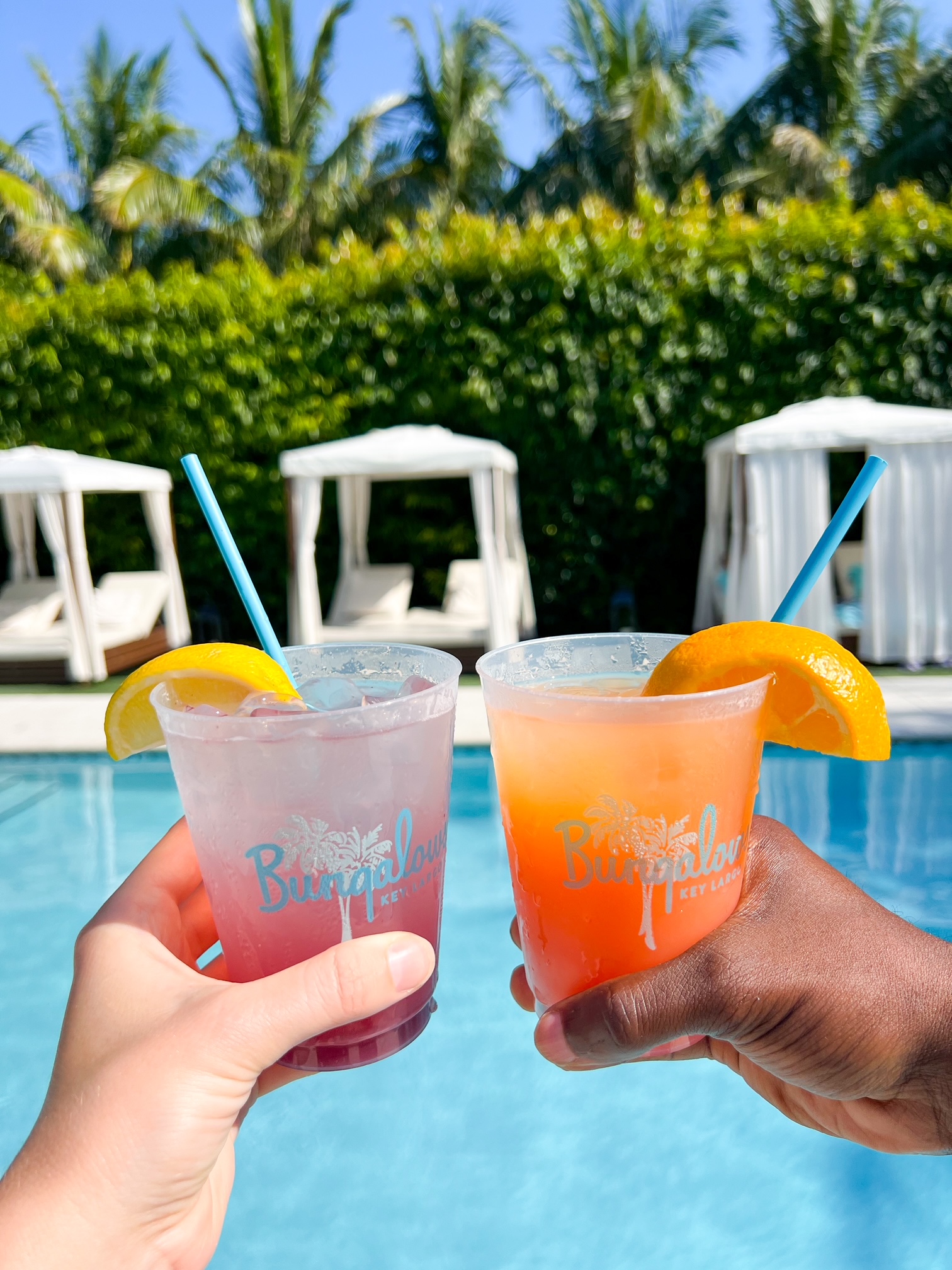 A picture of a couples hands holding drinks in the pool