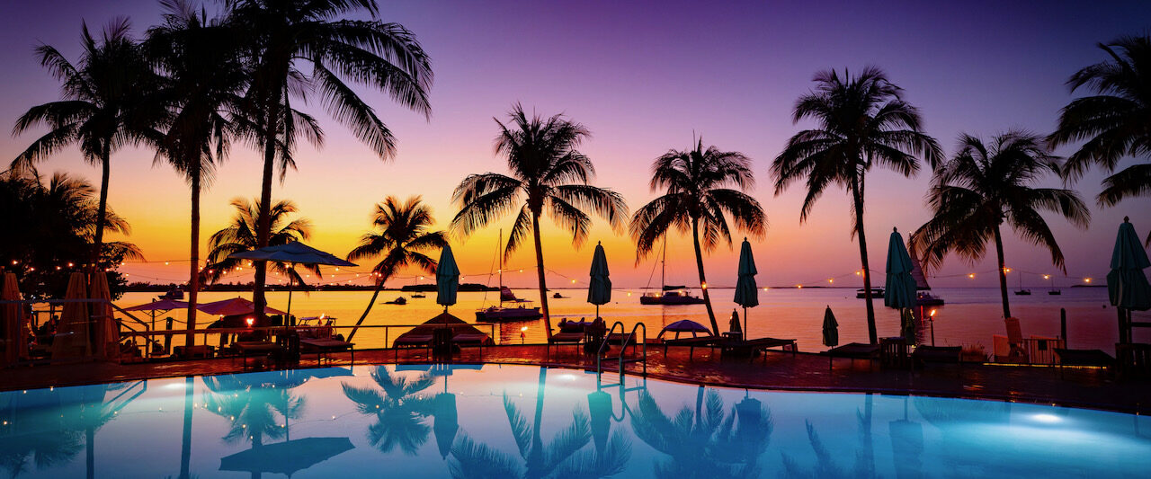 beautiful purple blue and orange sunset over a pool in florida with palm tree shadows