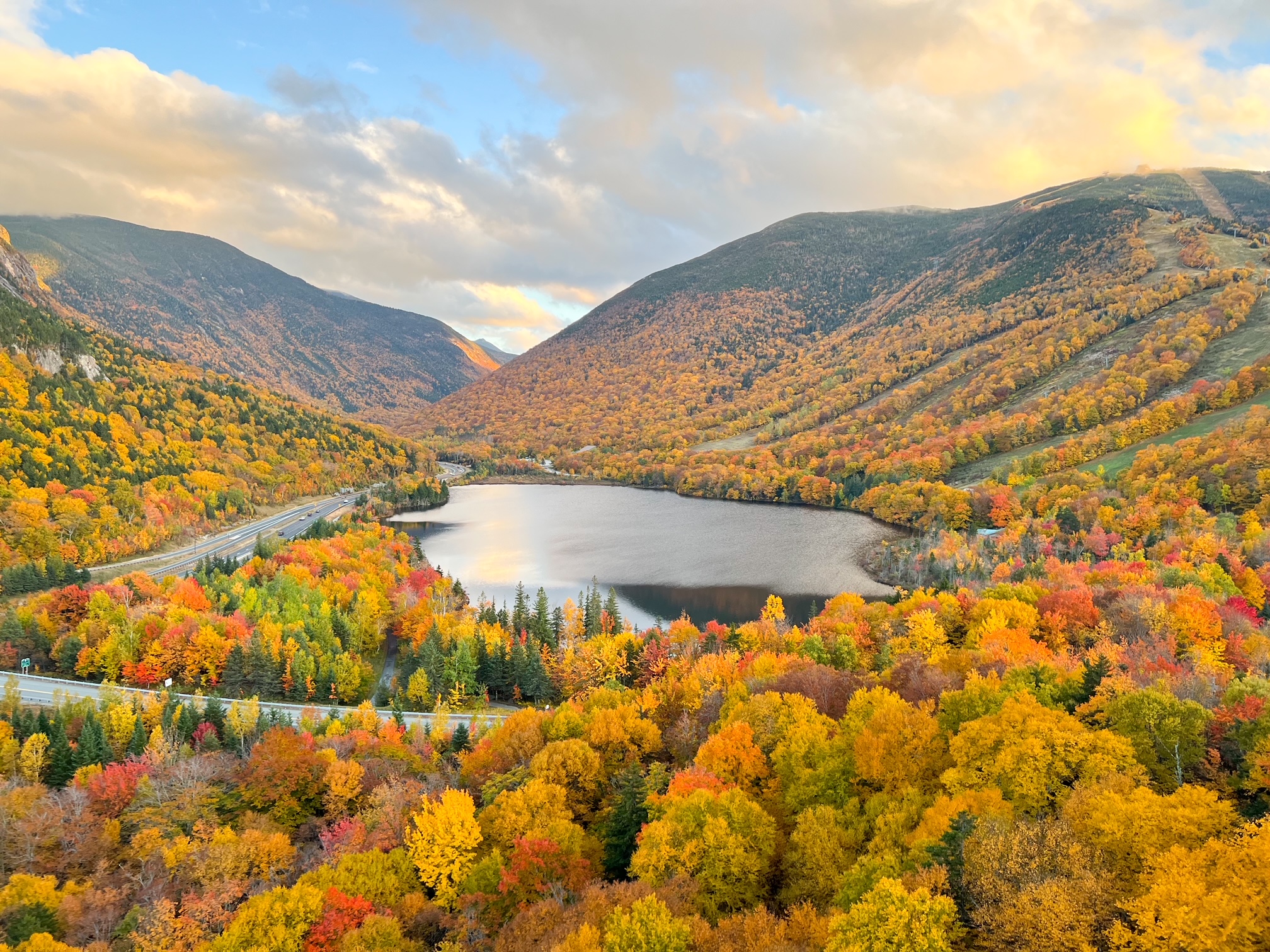 This photo shows the viewpoint of Artists's Bluff: the stunning mountains as they tilt inward over a lake and the trees are bright yellow and oranges. 