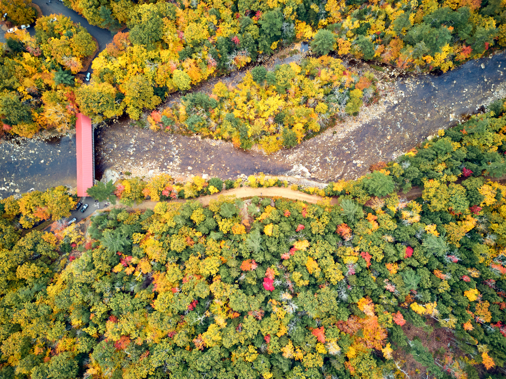 Another drone shot shows a covered bridge and the green and yellow trees surrounding it as as it crosses river. 