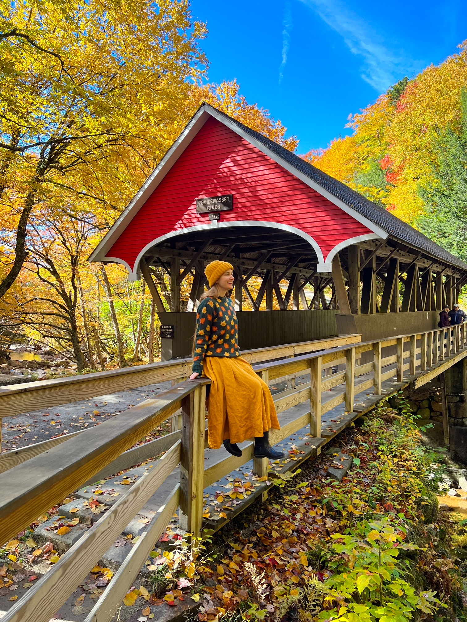 A  women sits on the edge of a bridge that has a cover over it, enjoying the views of Flume Gorge from a high point. 