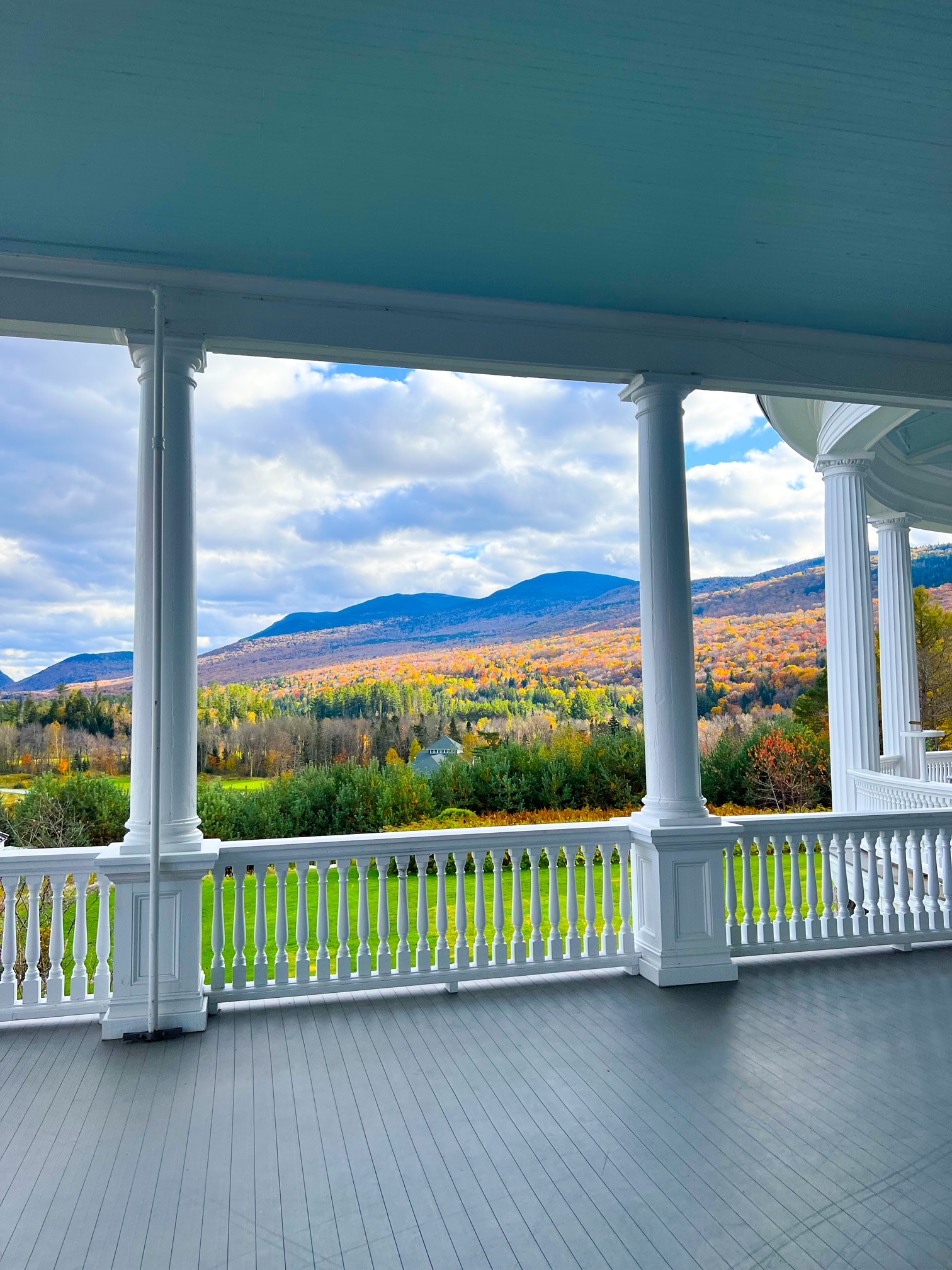 The white banner of the patio and porch of Omni Mount Washington Resort overlooks trees and mountains and is the place to stay when considering resorts for your New England Fall Foliage Road Trip Itinerary. 