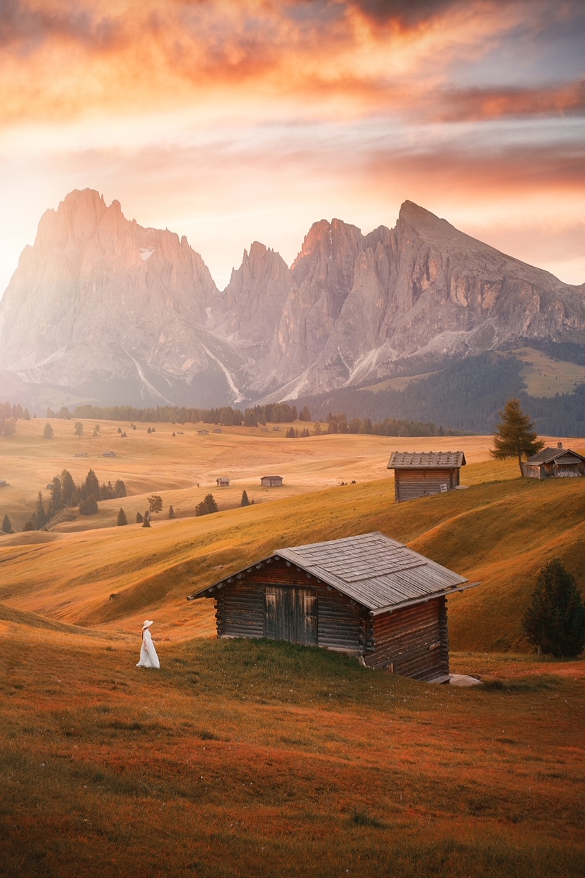 Girl walking with the mountains behind her. It is autumn and the girl is wearing a white dress. 