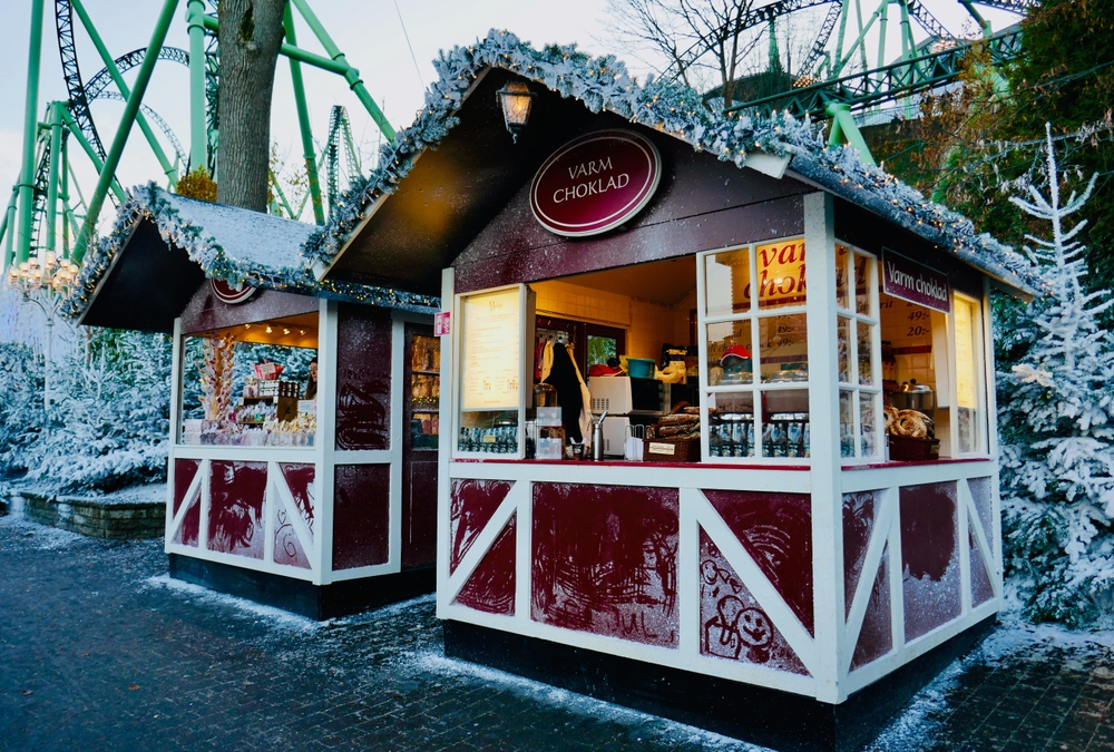 A specific wooden Chalet at the Gothenburg Christmas Market sells local and traditional cuisine and drinks, with a ride in the background: it is markets like these that make towns some of the best Christmas towns in Europe.