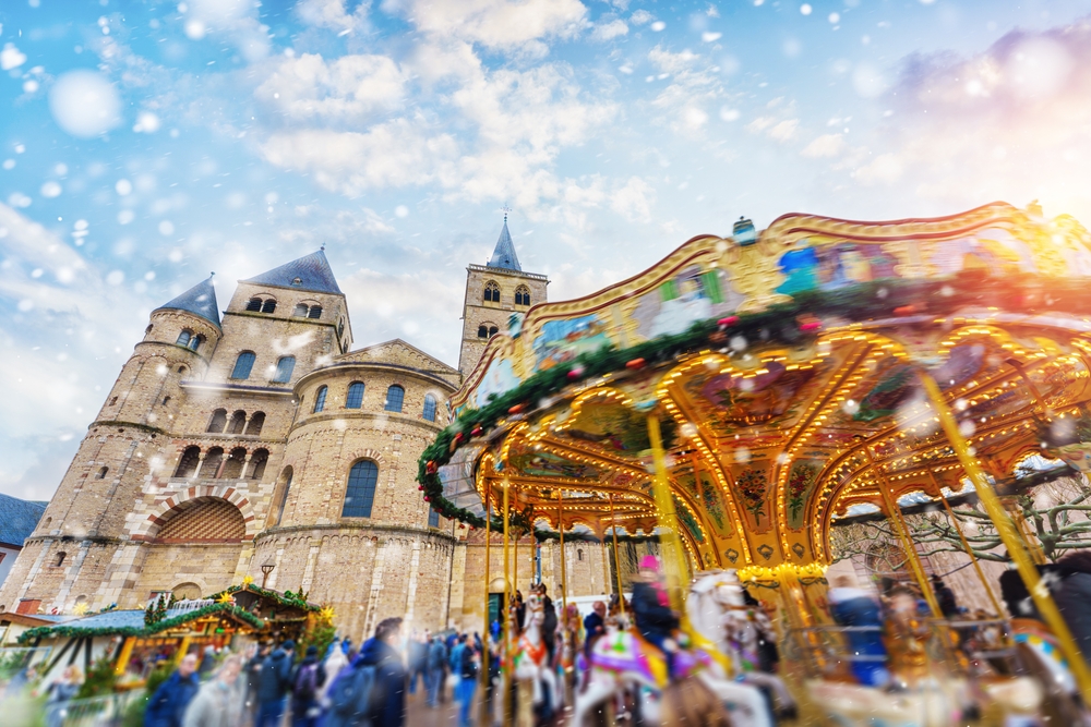 From a low-angle, one of the best Christmas towns in Europe, Trier, is shown with a blurred sensation: the castles in the back stand still but people and a carousel move at top speed in the white flurries of snow. 