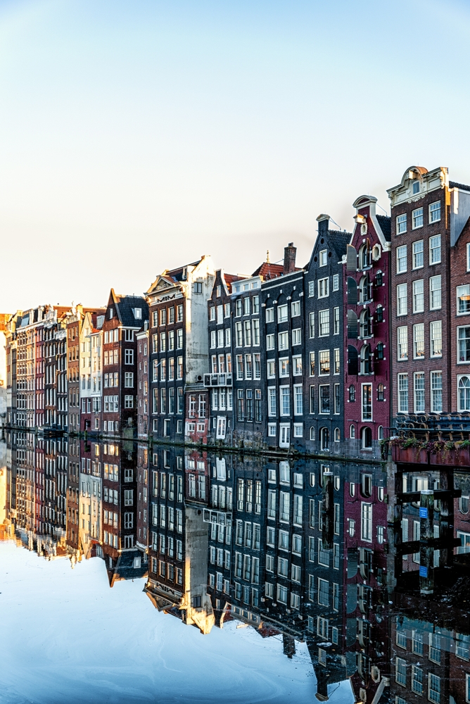 a row of different color houses on the water in amsterdam on a bright day 