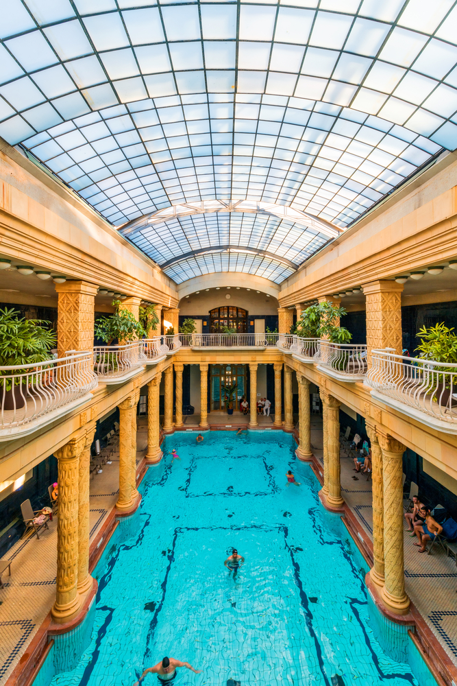 a budapest thermal spa indoors. people are in the water and there are columns on both sides of the pool