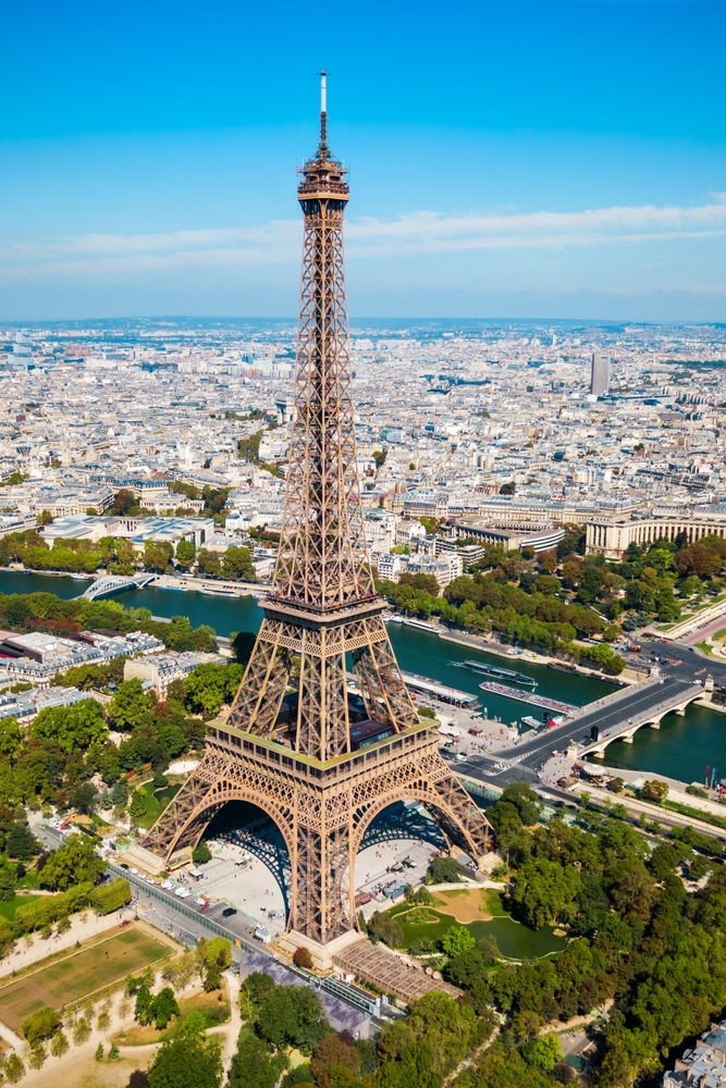 the eiffell tower stands tall in middle of image, the river seine, parks, buldings, and roads can be seen all around the tower 