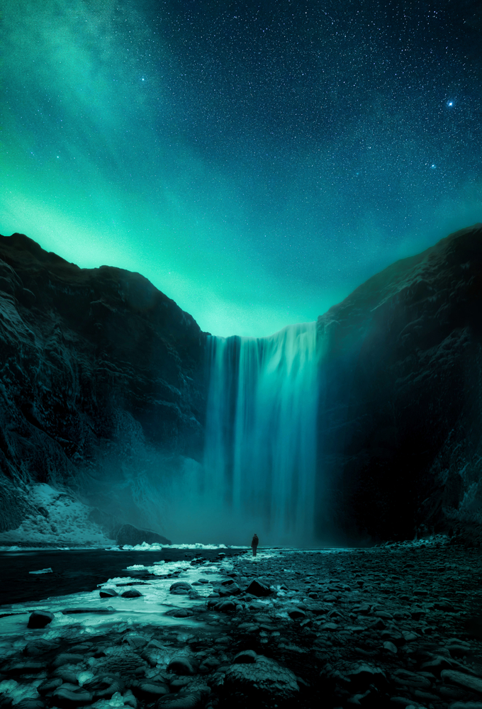 a person is standing in front of a large waterfall in iceland with the northern lights in the sky above 