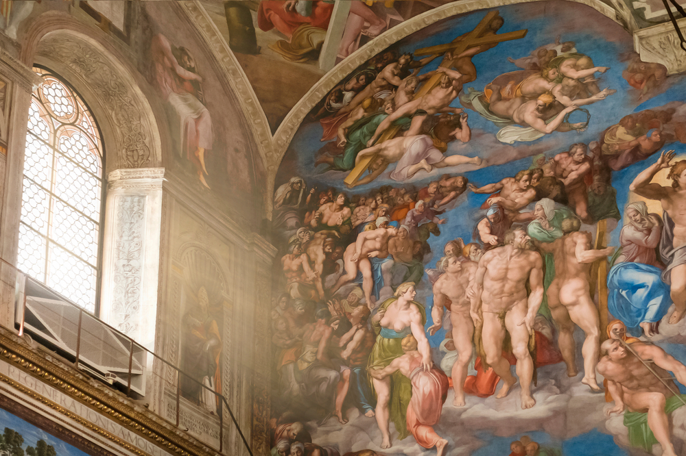 paintings on the wall and ceiling in the sistine chapel, there is a window on the left which is allowing light to shine inside