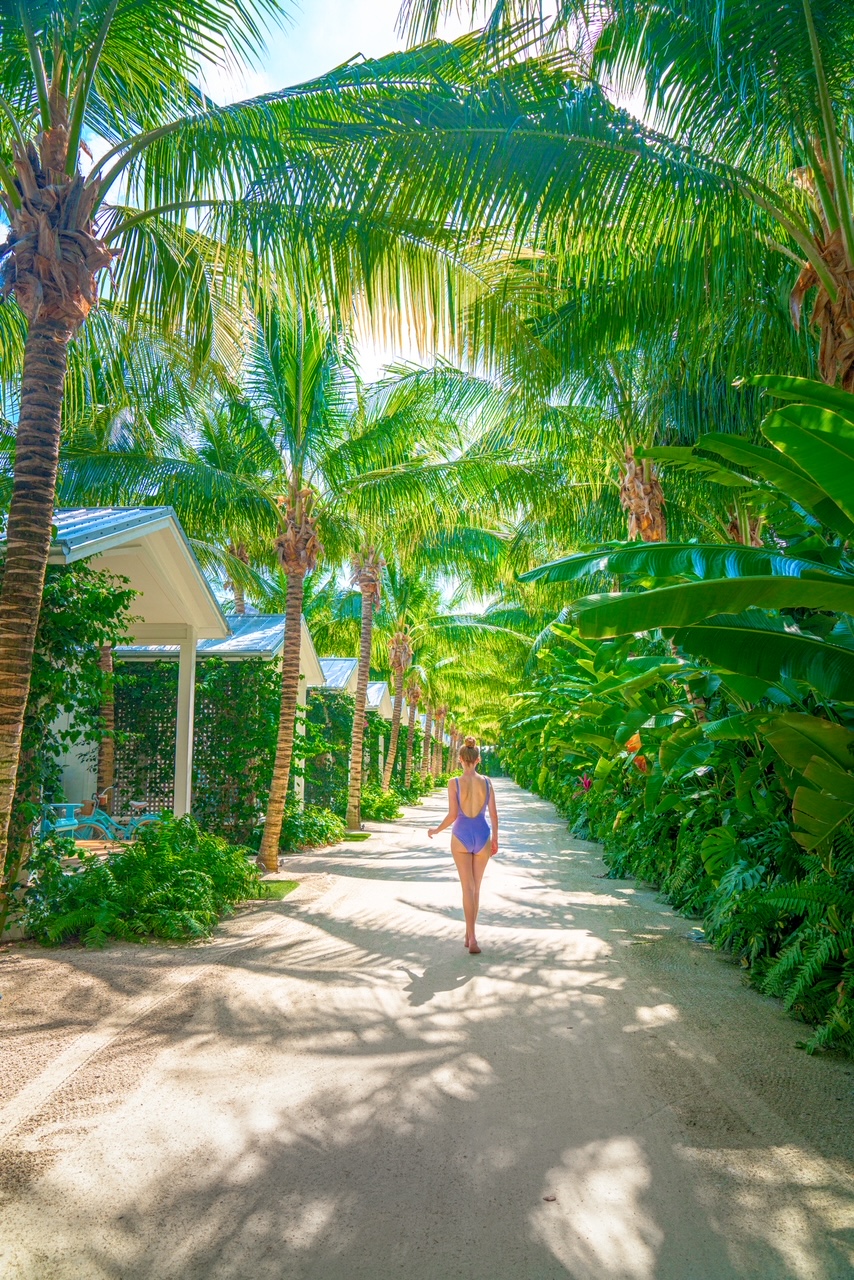 a girl in blue swimsuit walking under the palm trees in the Garden bungalows