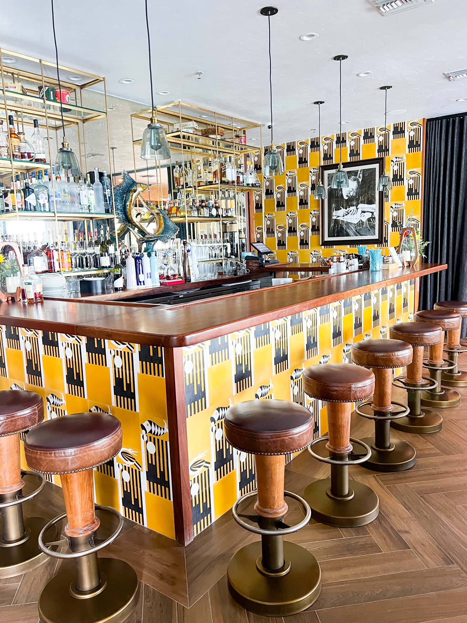 Hemingway Bar is popular for drinks with its wooden bar and stools with bright yellow wallpaper and hanging gold drink holders 