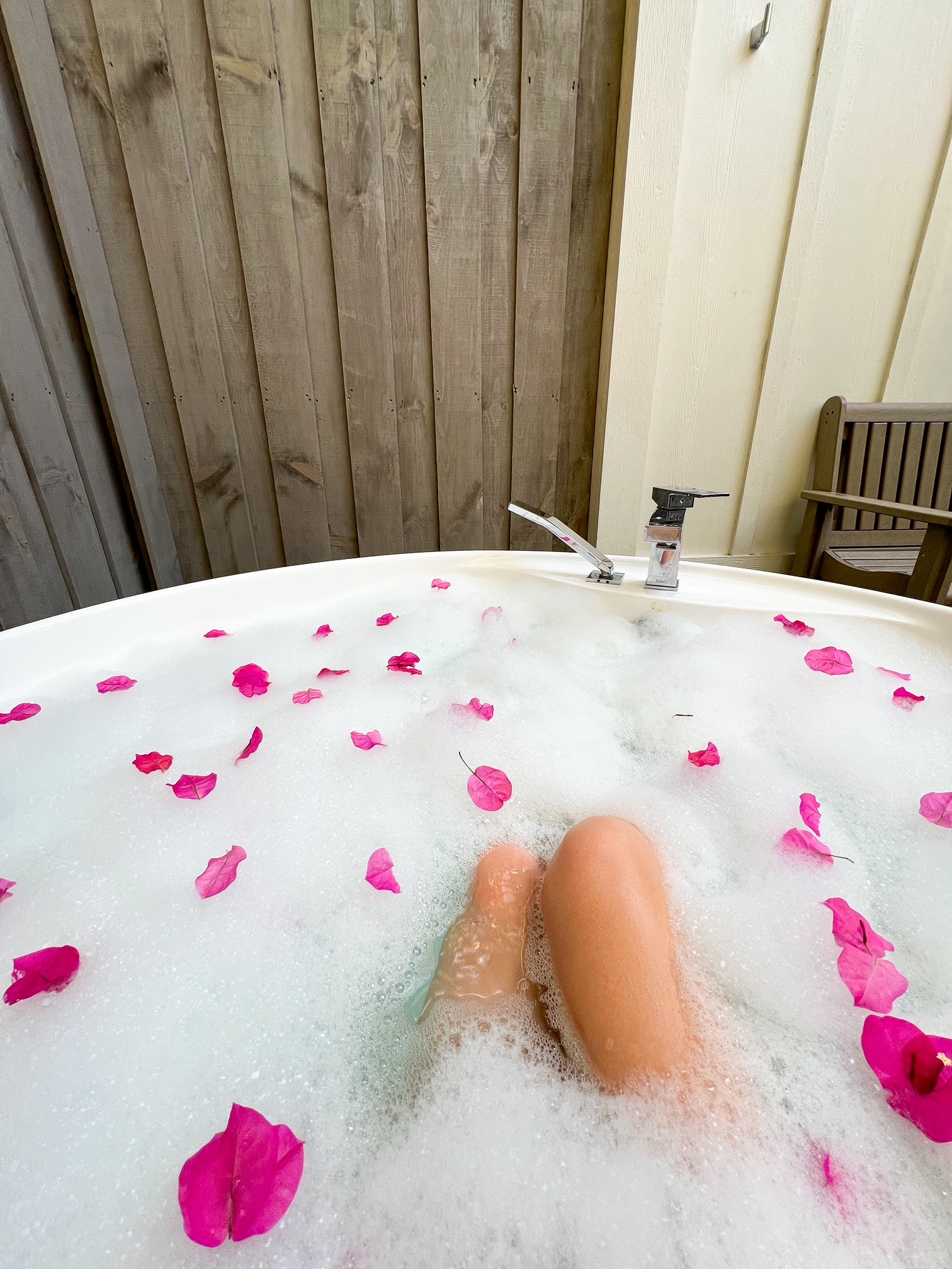 the outdoor soaking tub filled with bubbles and rose petals as a girls enjoys the tub