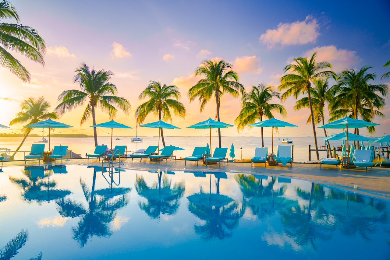 The sunset pool with palm tress, teal chairs and umbrellas, overlooking the ocean at sunset