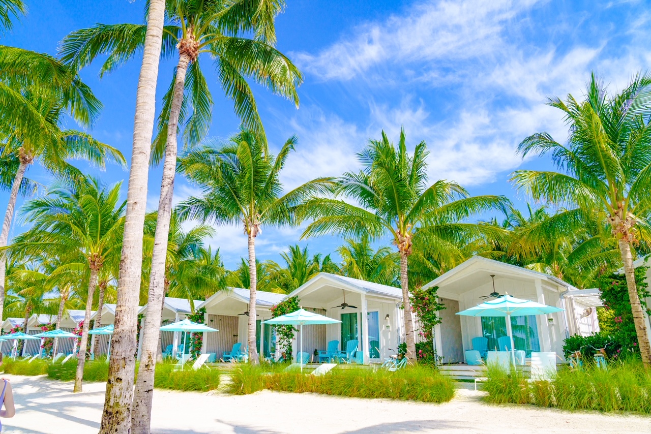 A view of the beachfront bungalows with palm trees, blue unbrealls and white bungalows