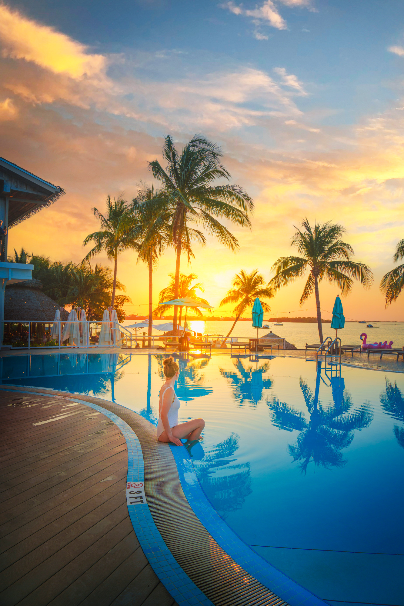 a girl in white swimsuit sitting poolside during the sunset at the Bungalows all inclusive resort sunset pool