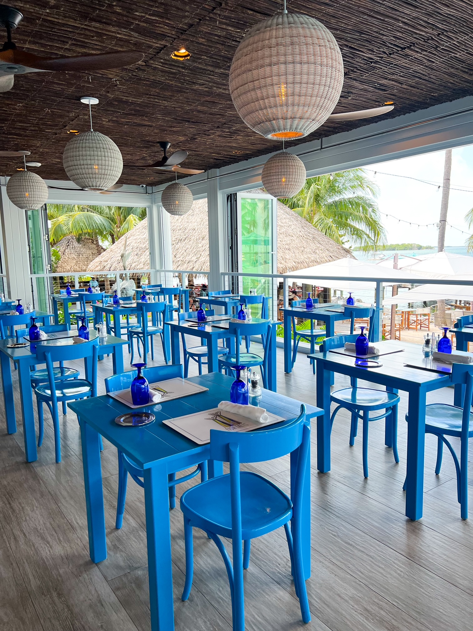 the inside of the tiki bar restaurant with blue stools and a thatched ceiling overlooking the sand